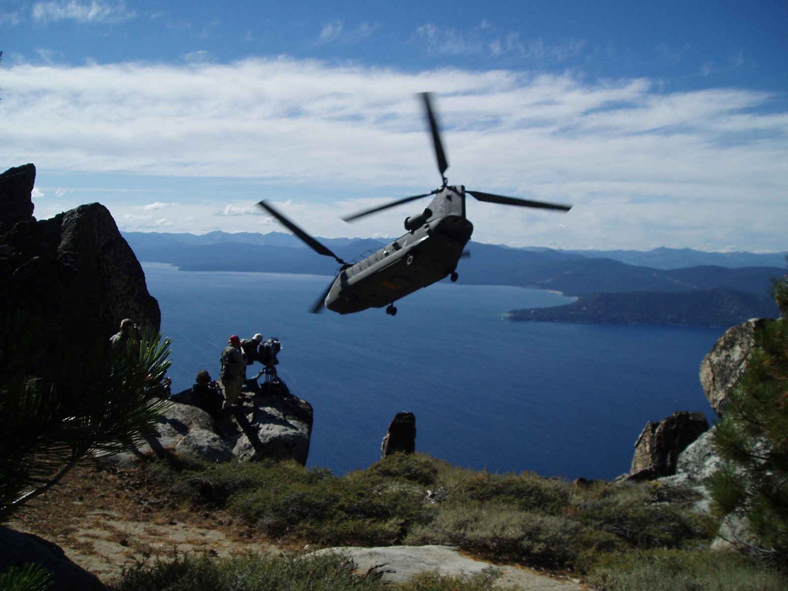 Film crew with IMAX camera on a cliff as a helicopter flies nearby over Lake Tahoe